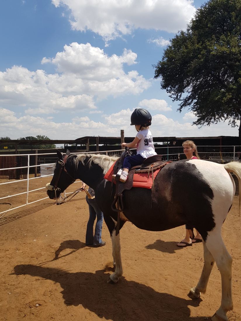 A child riding a pony with a helper walking alongside