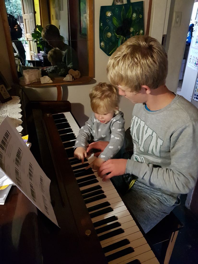 An older child helping a toddler press the keys of a piano